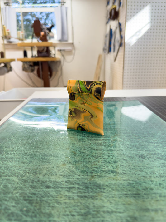 Green 1 leather wallet placed on a green surface, viewed from the front and back, with a workspace visible in the background where similar wallets are being created