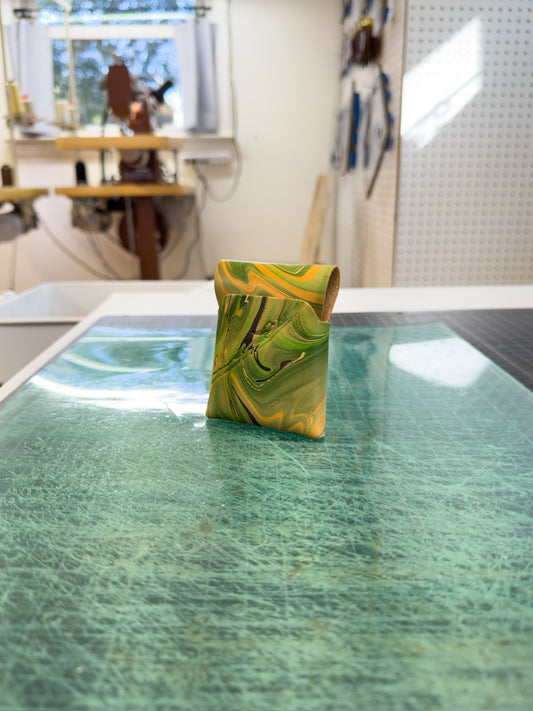 Green 2 leather wallet placed on a green surface, viewed from the front and back, with a workspace visible in the background where similar wallets are being created