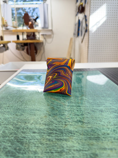 Rainbow 2 leather wallet placed on a green surface, viewed from the front and back, with a workspace visible in the background where similar wallets are being created