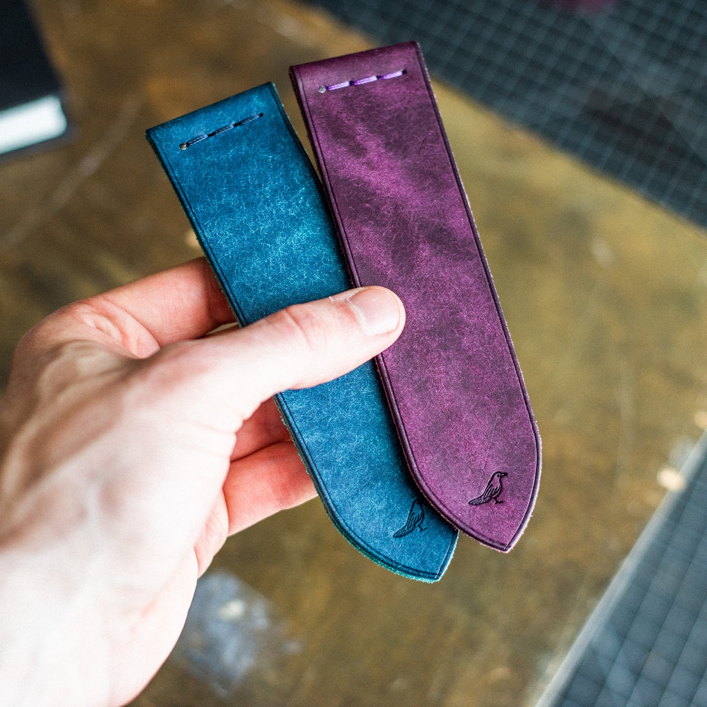 two bookmarks in violet and blue being held in the hand of a man with a blur background