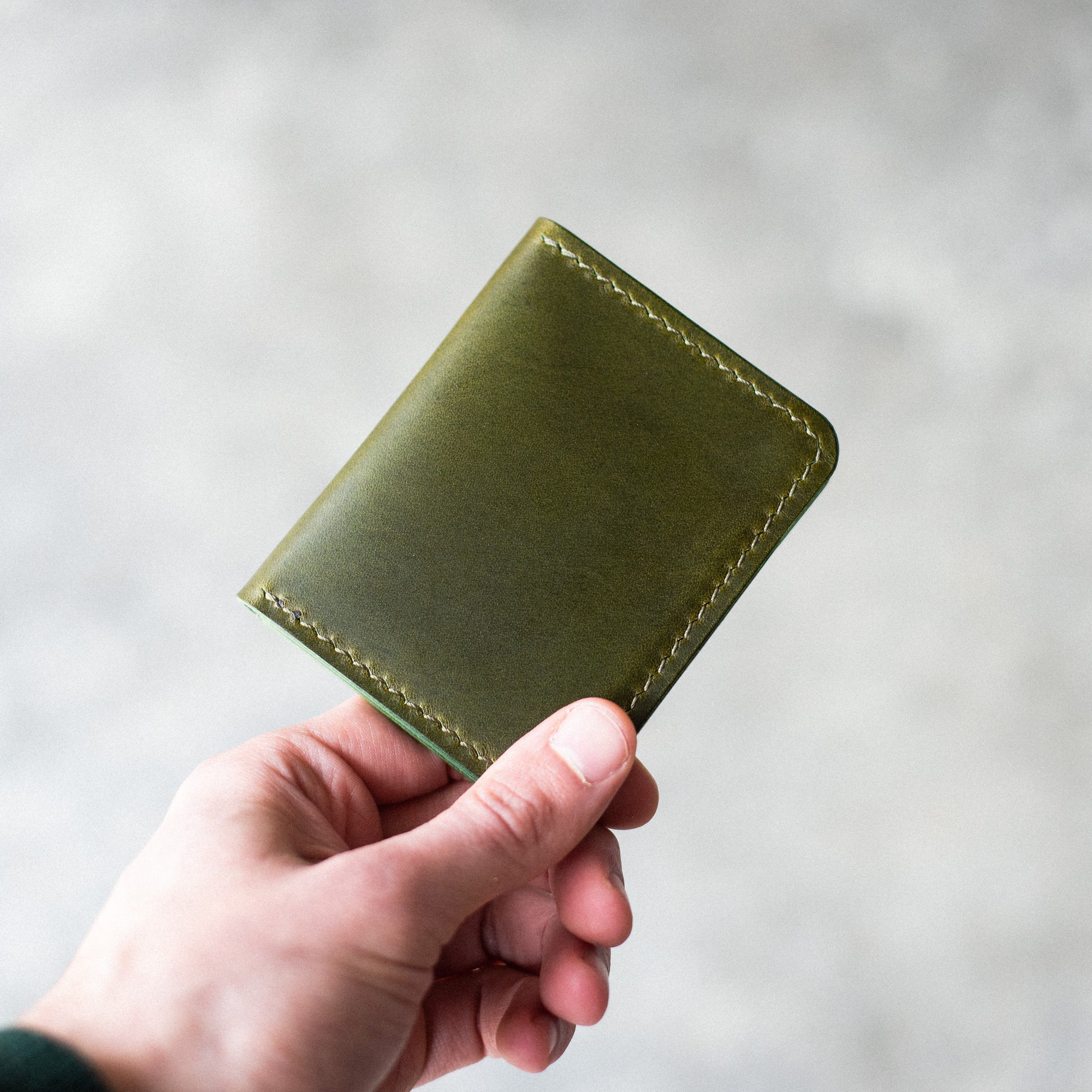 Closed Olive Pattern - Garrison Wallet held by a man against a blurred background.